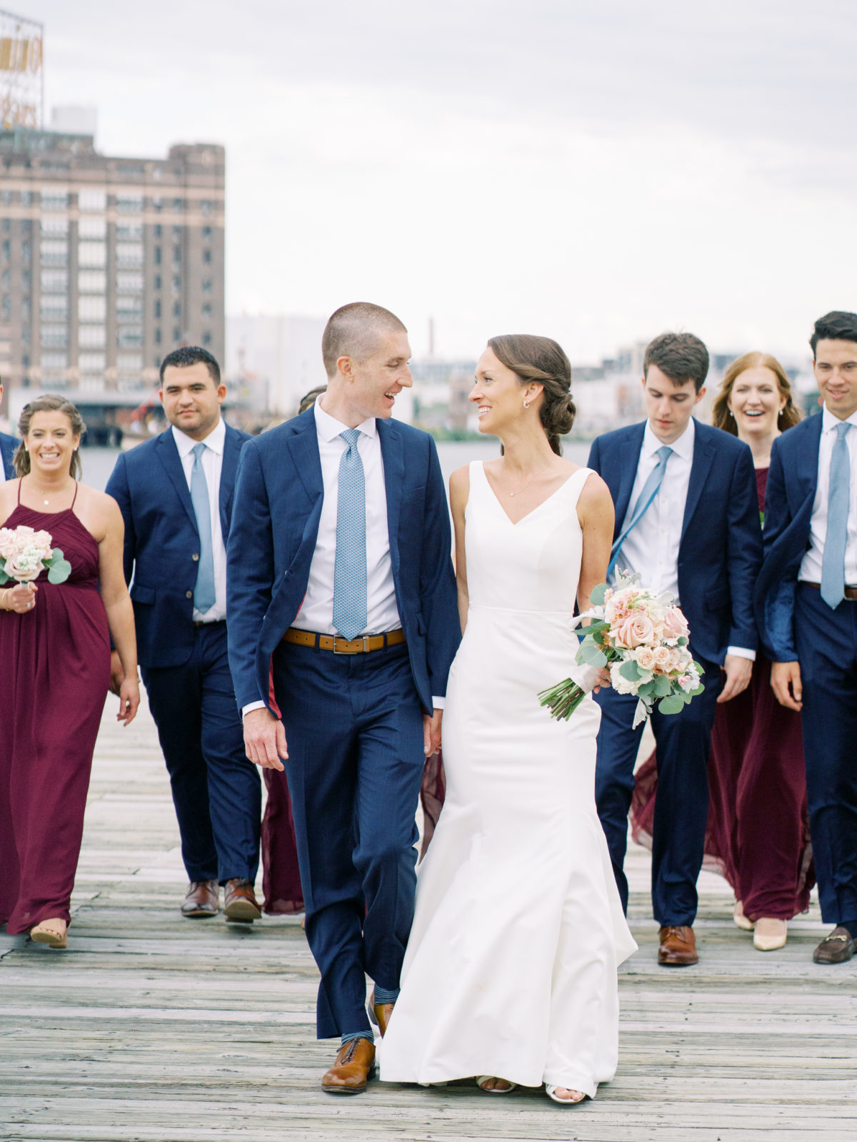 Bride and groom walk together with wedding party at Frederick Douglass-Isaac Myers Maritime Park in Baltimore Inner Harbor.