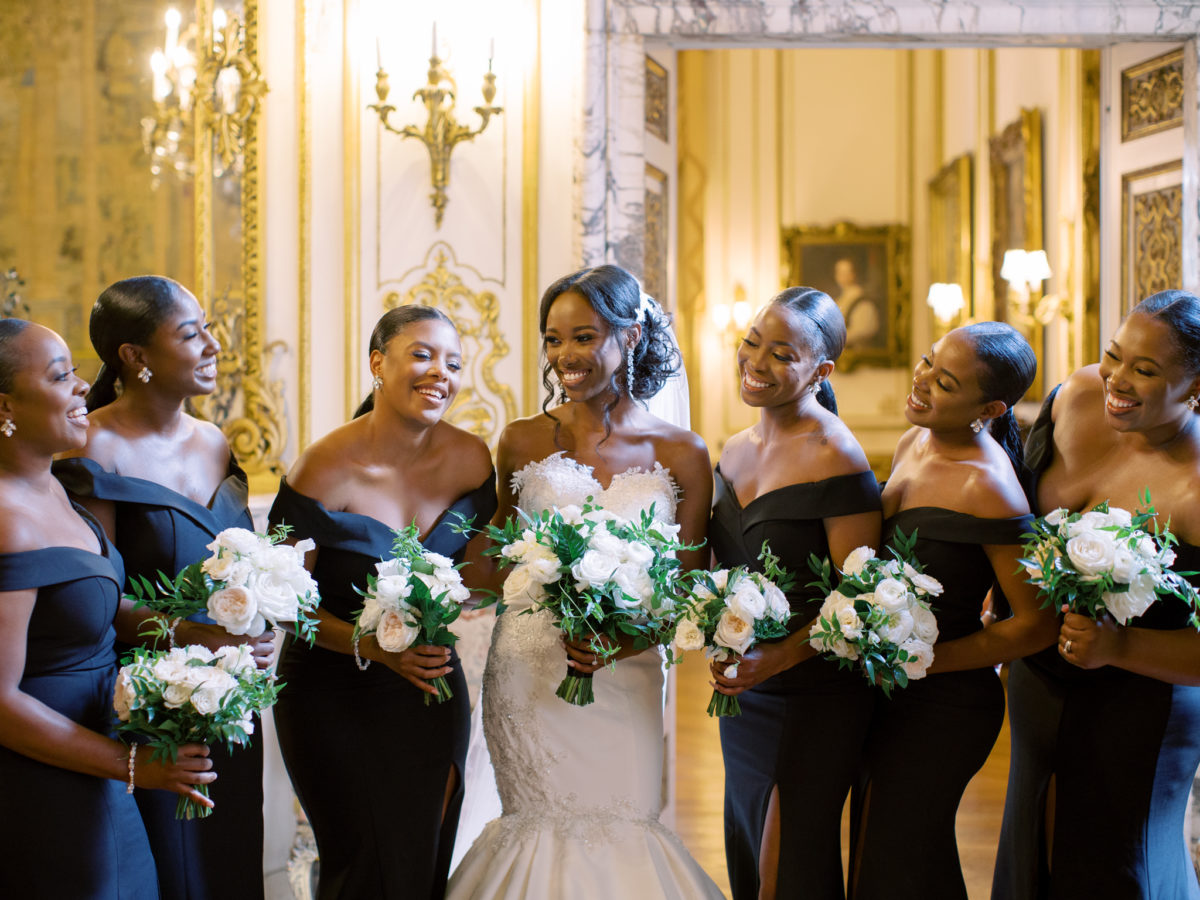 Bridesmaids in black satin off-the-shoulder dresses with white roses bouquets.